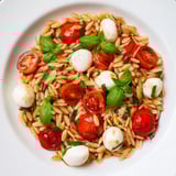 A colorful bowl of Caprese Orzo Salad, with fresh basil and cherry tomatoes glistening.