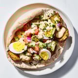 A warm pita pocket overflowing with vibrant Israeli Sabich, Israeli salad, and drizzled sauce.