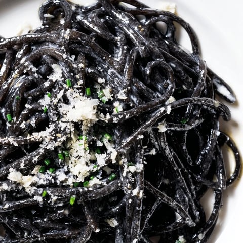 Squid Ink Pasta in a silky cream sauce is garnished with Parmesan and fresh chives for a dramatic presentation.