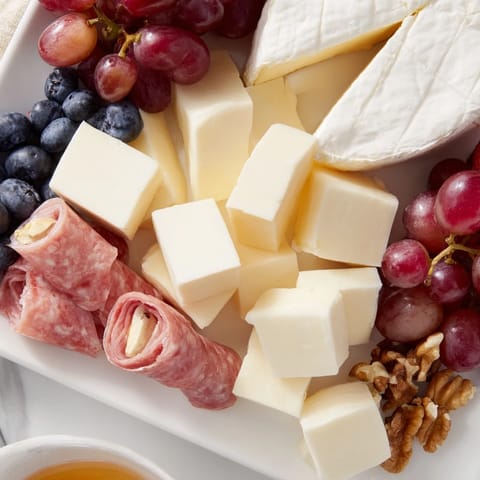 A vibrant Cozy Forest Animal Board displays cheeses, meats, and fruit artfully arranged for snacking.