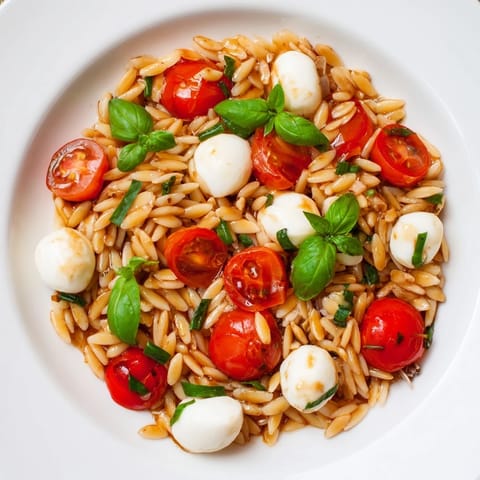 A colorful bowl of Caprese Orzo Salad, with fresh basil and cherry tomatoes glistening.