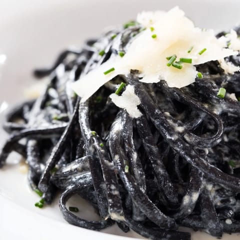 Twirls of black Squid Ink Pasta are coated in a glossy cream sauce beside bright lemon wedges.