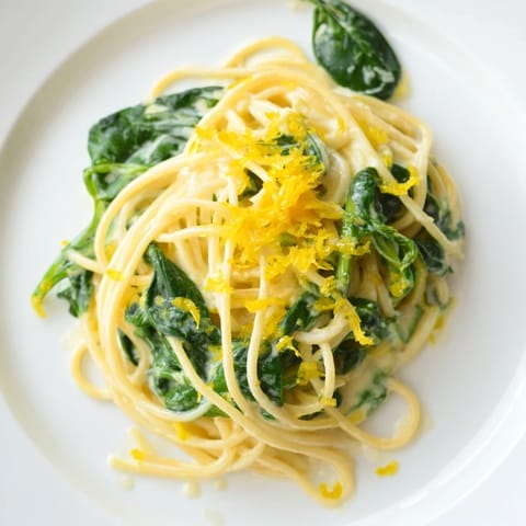 Freshly cooked Creamy Lemon Spinach Spaghetti twirled on a fork, showcasing silky cream sauce and bright green spinach leaves against a rustic table.