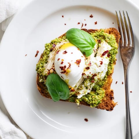 Fresh basil garnish and melted burrata crown crispy sourdough toast layered with savory pesto chicken, offering a gourmet snack ready in 25 minutes.