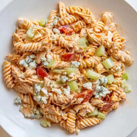 Chilled rotini pasta holds a zesty blend of buffalo sauce and sour cream, topped with crumbled blue cheese for extra tang.