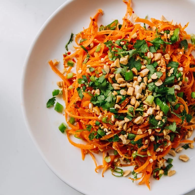 A colorful bowl brimming with Spicy Carrot Salad, garnished with sesame seeds and chopped peanuts.