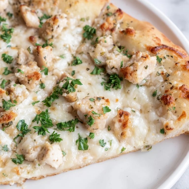 A sliced Chicken Alfredo Pizza on a wooden board, showcasing the cheesy pull and savory chicken toppings, perfect for a weeknight Italian-American dinner.