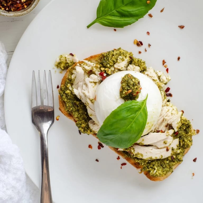 A close-up of Pesto Chicken Burrata Toast shows juicy chicken, melted cheese, and herbaceous pesto on crunchy bread, ideal for a quick lunch.
