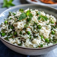 A fragrant rice pilaf with sweet spring peas, fresh mint, and bright lemon zest, served as a vibrant vegetarian side dish.